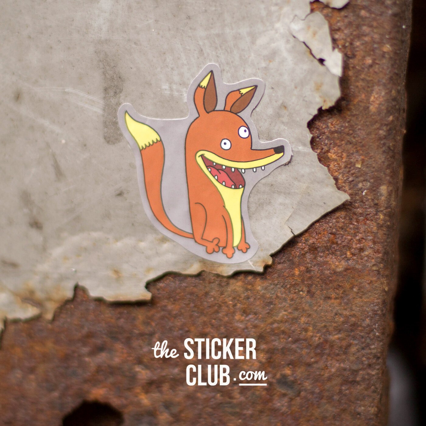 The Sticker Club fox character as a die-cut sticker, stuck to rusty painted metal